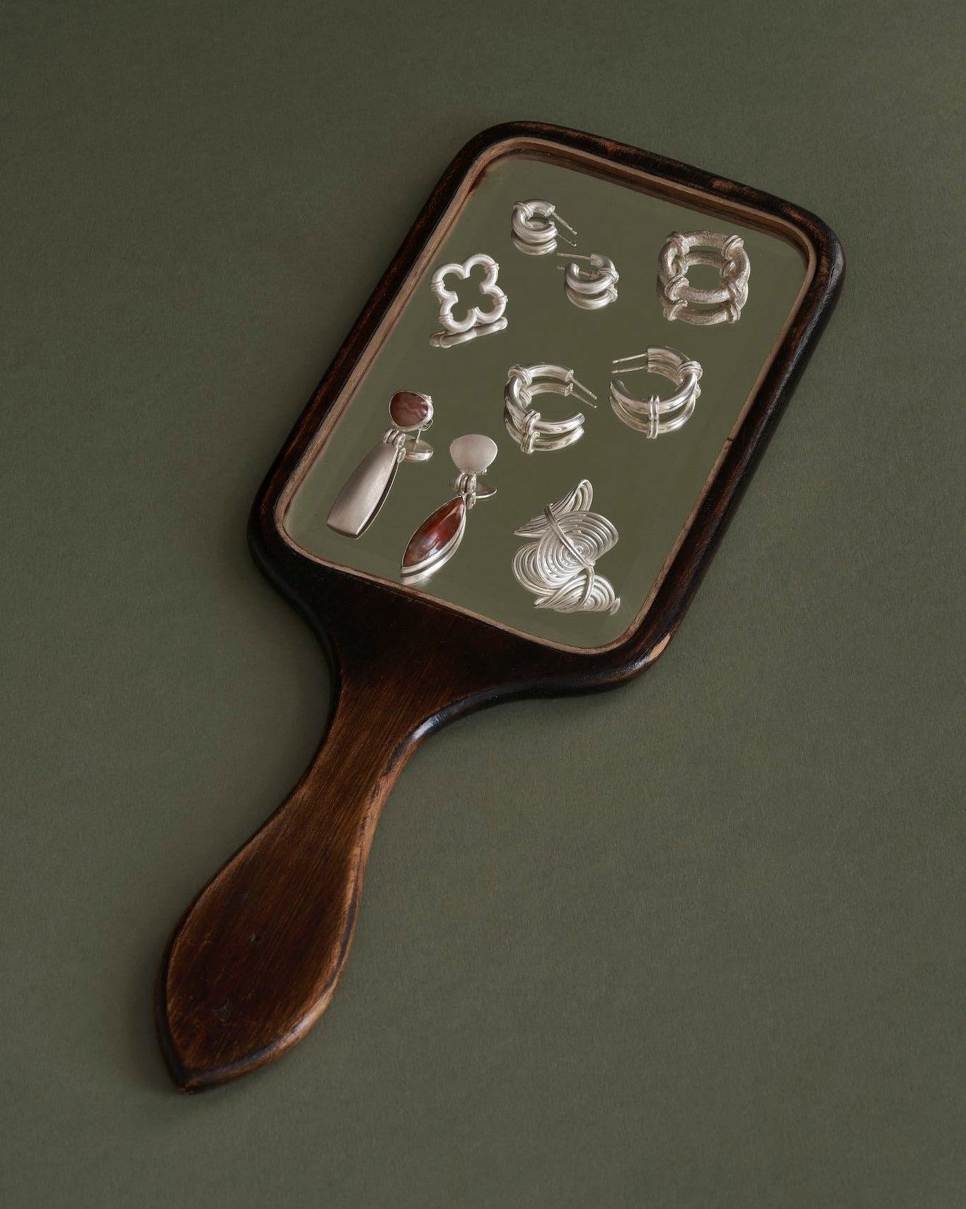 Handheld mirror with jewellery on a green background
